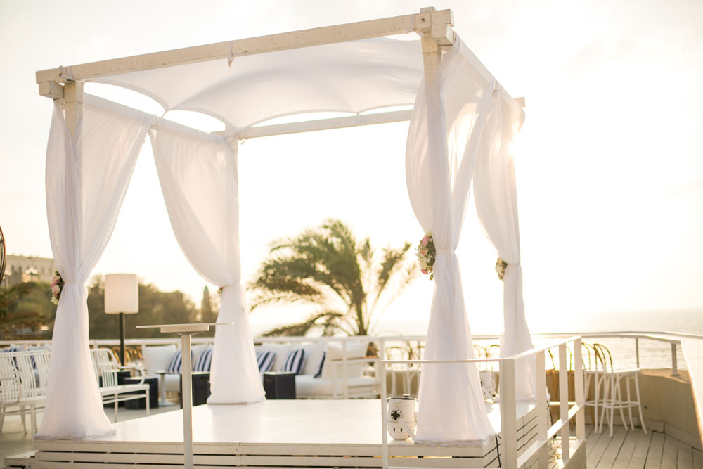 Two women getting married under a pergola with plants and sunshine, celebrating their love and commitment to each other.