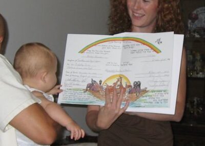 A father holds his newborn baby while the mother presents a baby naming certificate at a ceremony officiated by Rabbi Cantor Ron Broden.