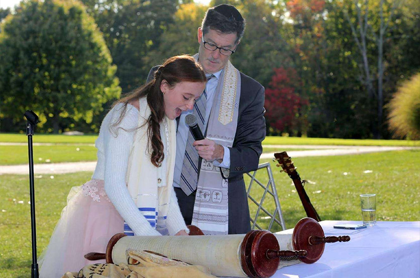 Rabbi Ron Broden holding a microphone for a young girl at her bat mitzvah.